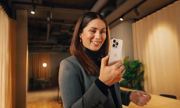 Hymyilevä liikenainen käyttää iPhone 16 Pro -puhelintaan