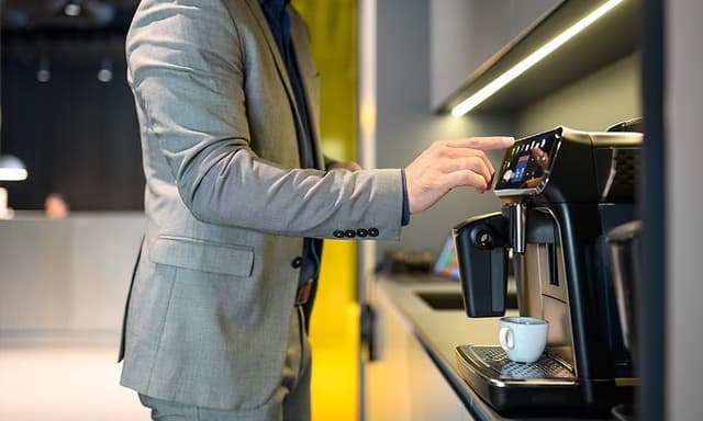 Mies valmistaa kahvia automaattisella kahvikoneella, jossa erillinen maidonvaahdotin