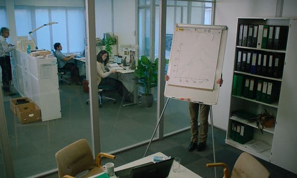 Mies piileskelee neuvotteluhuoneen fläppitaulun takana