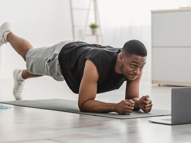 Hjemmetræning: En mand i plankeøvelse på yogamåtte derhjemme