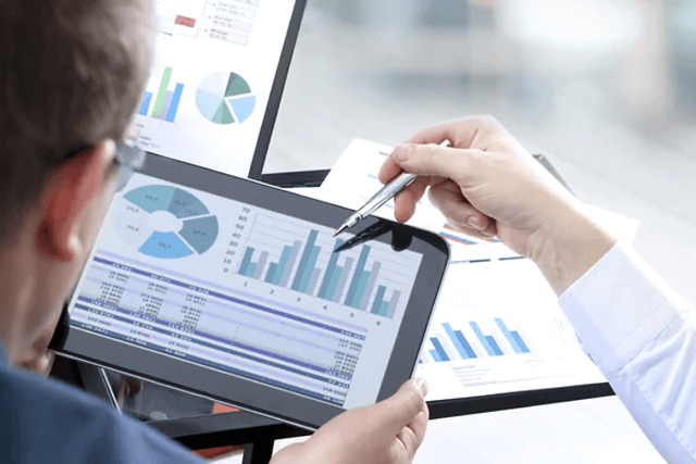 Hånd bruger kuglepen til at vise statistikker på en tablet til kollega