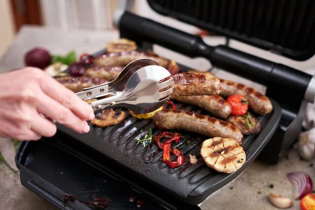 Mann griller pølser og grønnsaker på en elektrisk grill