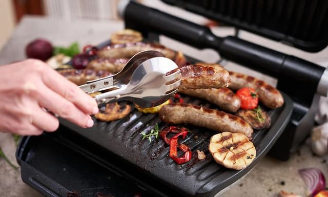 Mann griller pølser og grønnsaker på en elektrisk grill