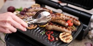 Henkilö grillaa lihaa ja kasviksia sähkögrillillä