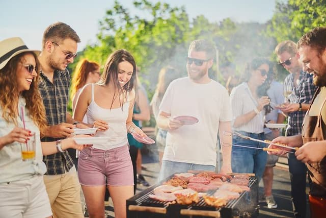 People gathered around a grill serving themselves and having a good time