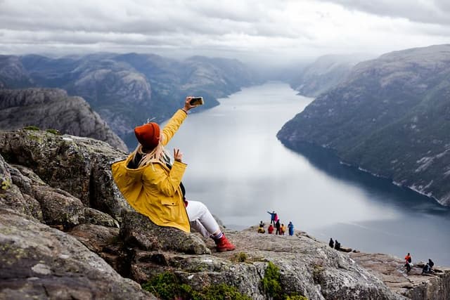 Happy woman hiker sits on the top of the Preikestolen mountain