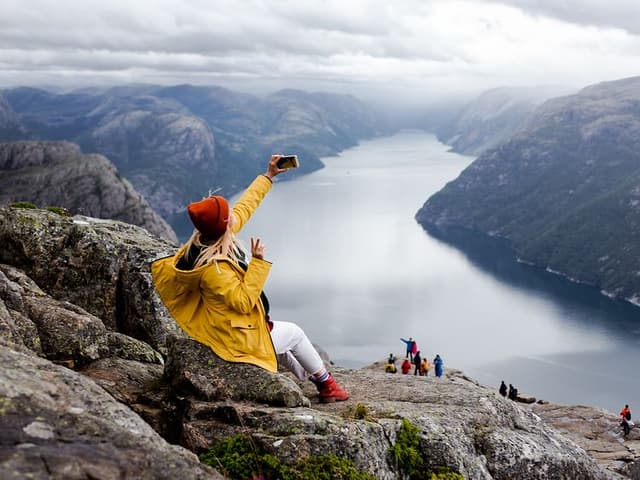 Happy woman hiker sits on the top of the Preikestolen mountain