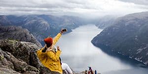 Happy woman hiker sits on the top of the Preikestolen mountain