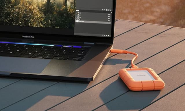 På ett campingbord ligger en laptop med en extern hårddisk inkopplad samt kamerautrustning