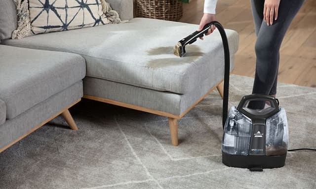 A Bissell carpet cleaner in use, cleaning a beige carpet with visible water and cleaning solution.