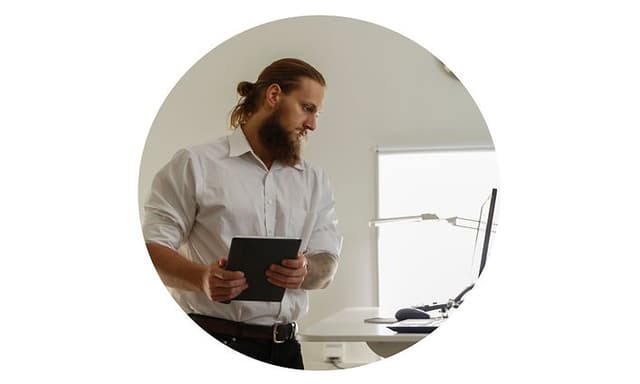 B2B - Trade-in - Man standing in the office looking at the laptop on the desk-Round