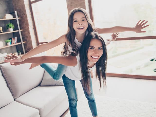 Indoor Climate hero banner with a girl and a mother pretending to fly together in the living room