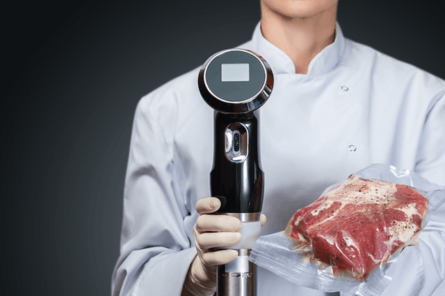Sous Vide - A chef holding a vacuum meat and sous vide circulator in her hands