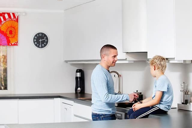 Mies laittaa ruokaa pojan istuessa keittiön työtasolla