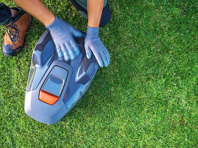 A Person Services a Robotic Lawn Mower on a Lush Green Lawn During Daylight