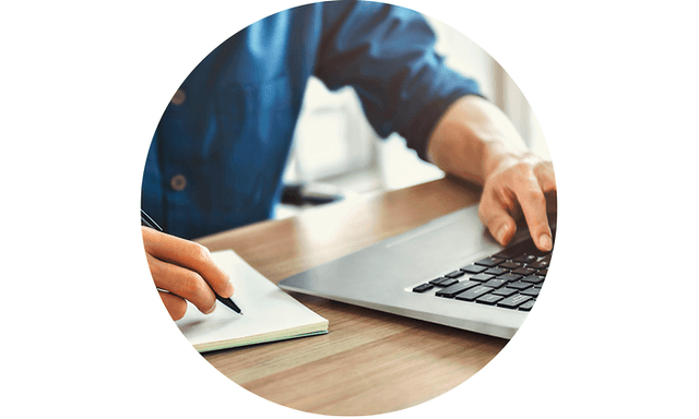 Man working on a laptop and taking notes on paper