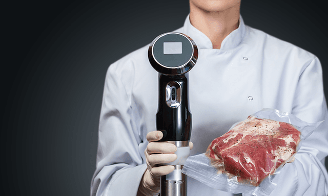 En kok holder sous vide-cirkulationspumpe og vakuumpakket kød