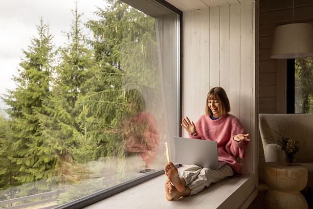 Internet i sommerhus: Kvinde sidder med laptop i vindue i sommerhus