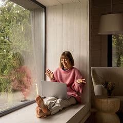 Internet i sommerhus: Kvinde sidder med laptop i vindue i sommerhus
