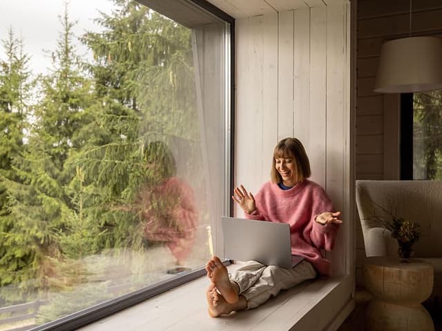 Internet i sommerhus: Kvinde sidder med laptop i vindue i sommerhus