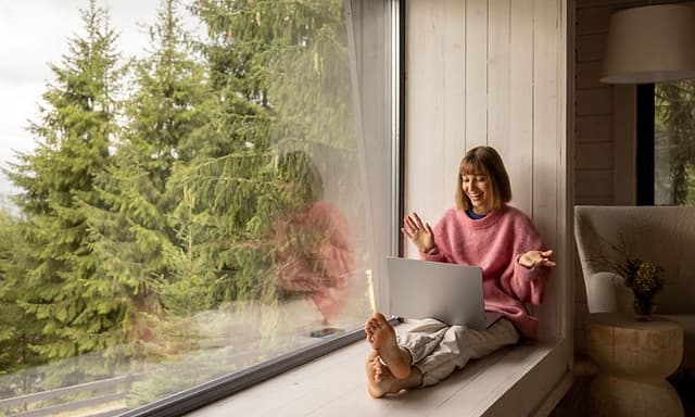 Internet i sommerhus: Kvinde sidder med laptop i vindue i sommerhus