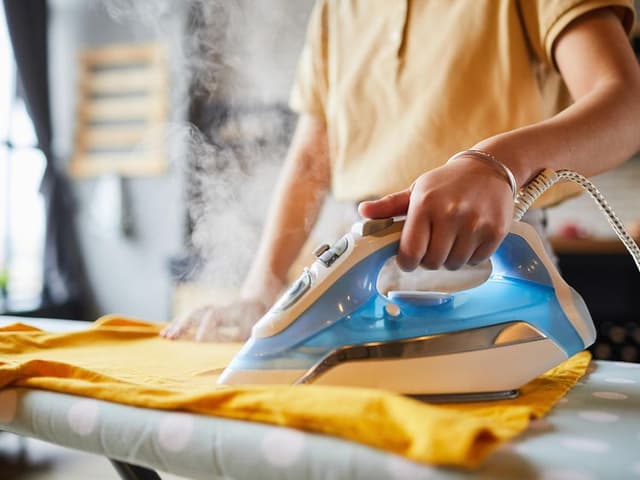 Bedste dampstrygejern: Strygejern anvendes af person på krøllet tøj