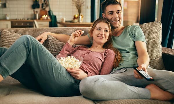 Pariskunta rentoutuu sohvalla televisiota katsellen ja syö popcornia