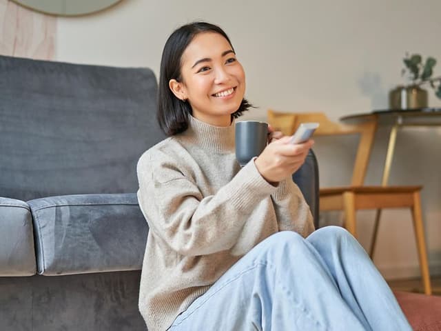 Kvinde med fjernbetjening sidder på gulvet foran sofa