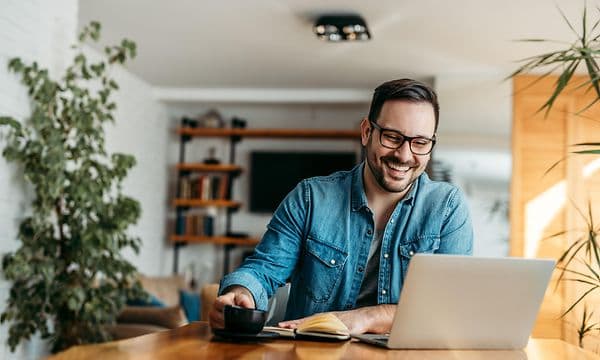 Mand sidder smilende ved sin laptop
