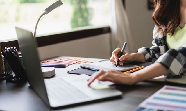 Naissuunnittelija työskentelee tietokoneellaan graafisen työn parissa