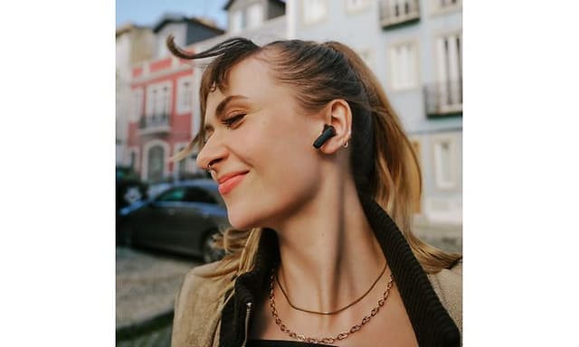 Sennheiser ACCENTUM Open øretelefoner i ørerne på en glad kvinde i by