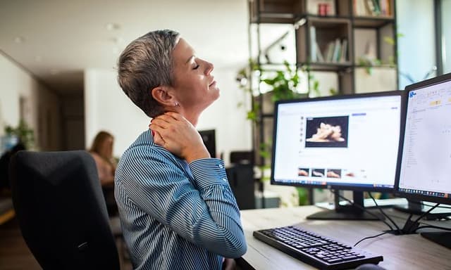 Kvinde holder om sin ømme nakke, mens hun arbejder på kontor