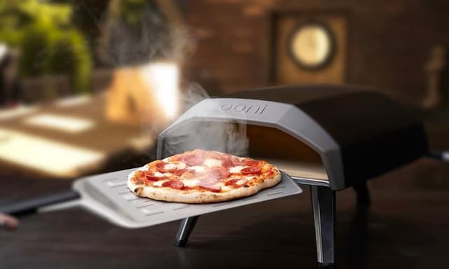 Ooni Koda 12 -pizzauuni, josta henkilö on ottamassa ulos valmista pizzaa