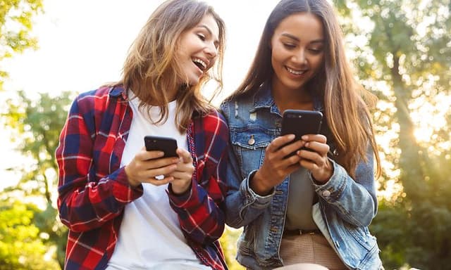 Billige smartphones i hænderne på to smilende unge kvinder