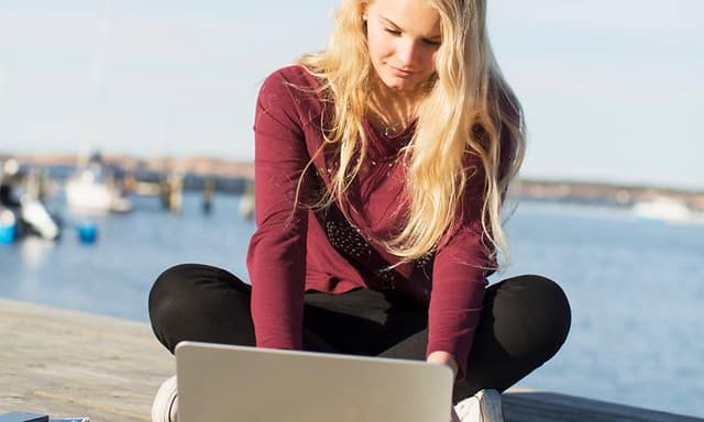 Ung kvinne sitter på en brygge og jobber med den bærbare datamaskinen sin