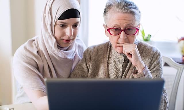 Yngre kvinne hjelper en eldre kvinne med å bruke bærbar PC