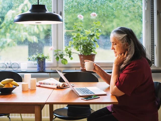 Computing - AI PC - Older woman sitting by kitchen table using her laptop