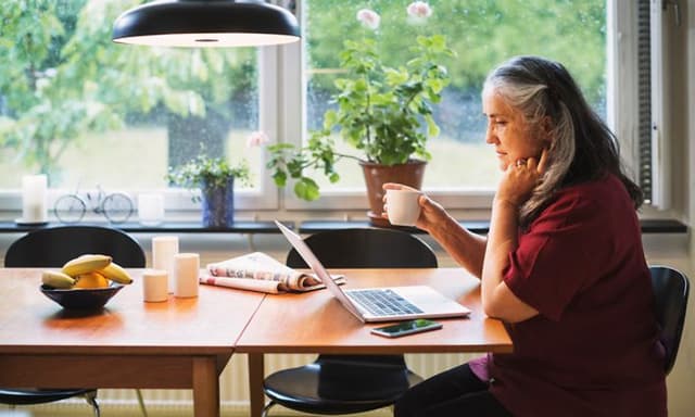 Computing - AI PC - Older woman sitting by kitchen table using her laptop