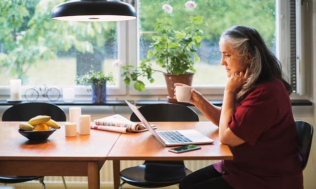 Computing - AI PC - Older woman sitting by kitchen table using her laptop