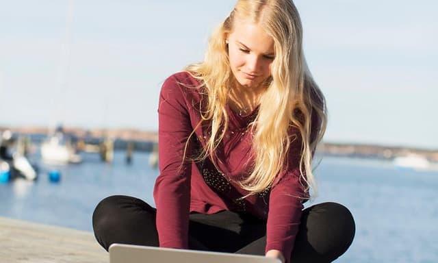 Computing - AI PC - Young woman sitting on a pier working with her laptop