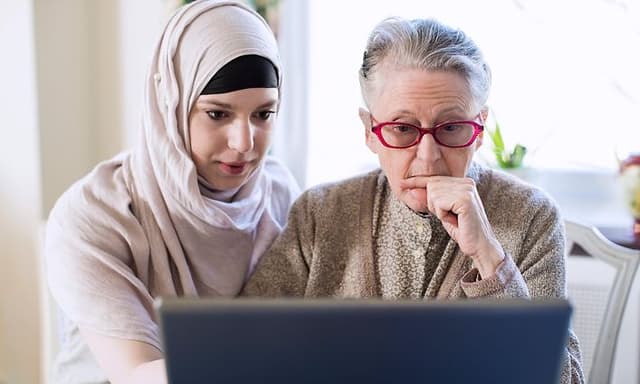 Yngre kvinde hjælper en ældre kvinde med at bruge en laptop