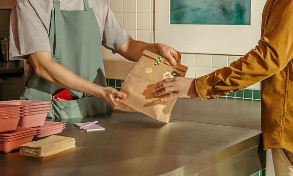 Cafémedarbejder rækker kundens ordre over disken