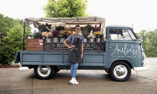 Leende kvinna som står bredvid sin lilla blomsterbutik i en lastbil