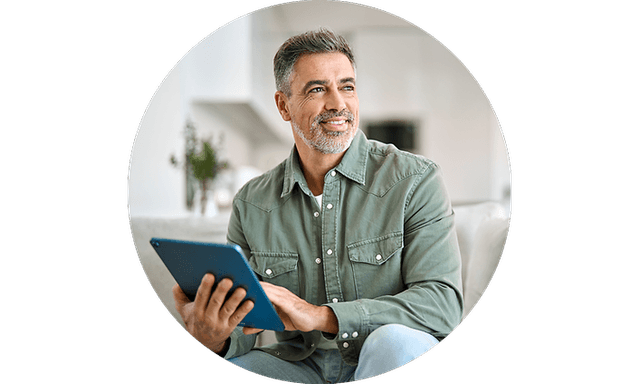 Smilende mand sidder på en sofa og arbejder på sin tablet