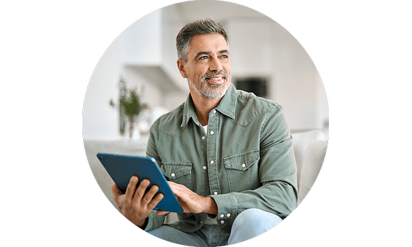 Mies istuu sohvalla ja käyttää tablet-laitettaan