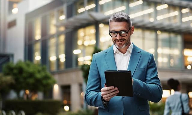 Mies seisoo yrityksen ulkopuolella ja työksentelee tabletillaan