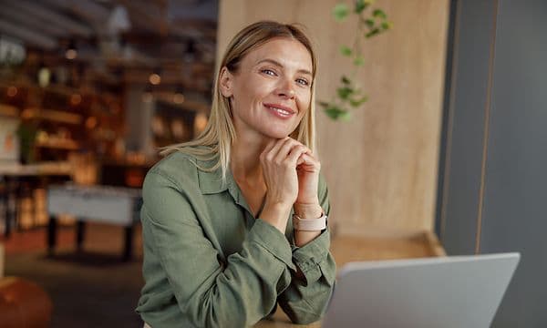 Smilende kvinne sitter ved en bærbar PC