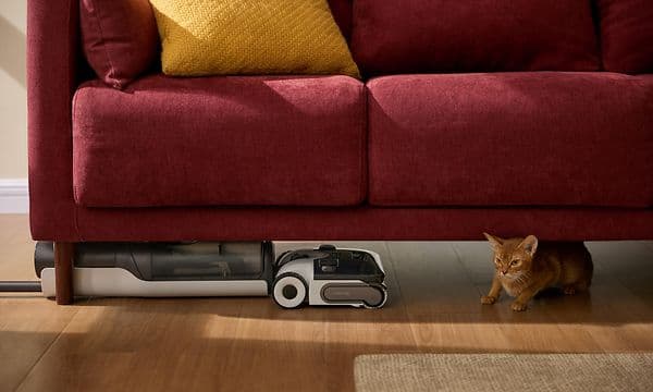 Roborock F25 ACE under en rød sofa sammen med en kat