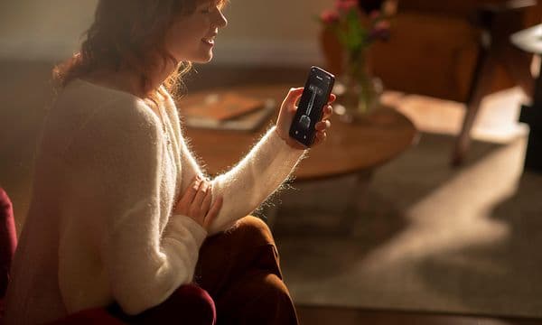 Kvinne sitter i en lenestol og bruker mobilen til å styre en trådløs støvsuger