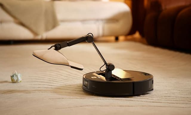 Robotstøvsuger med mekanisk arm løfter tøffel fra teppe.